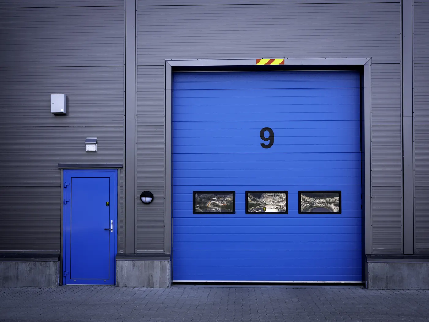 Blå industriport merket 9 med gangdør ved siden av, i mørk fasade