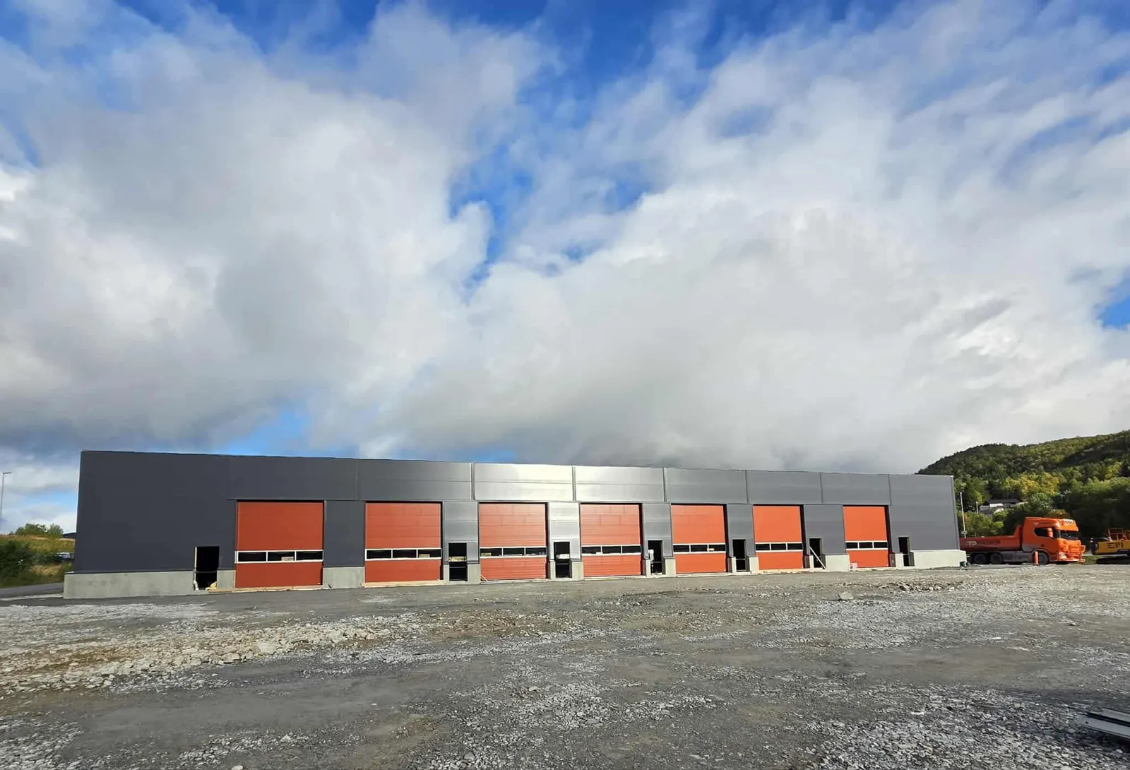 Lang industrihall med en rekke oransje porter under skyet himmel